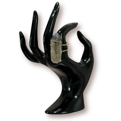 Raw smoky quartz crystal ring wrapped in gold wire, displayed on a glossy black ring stand